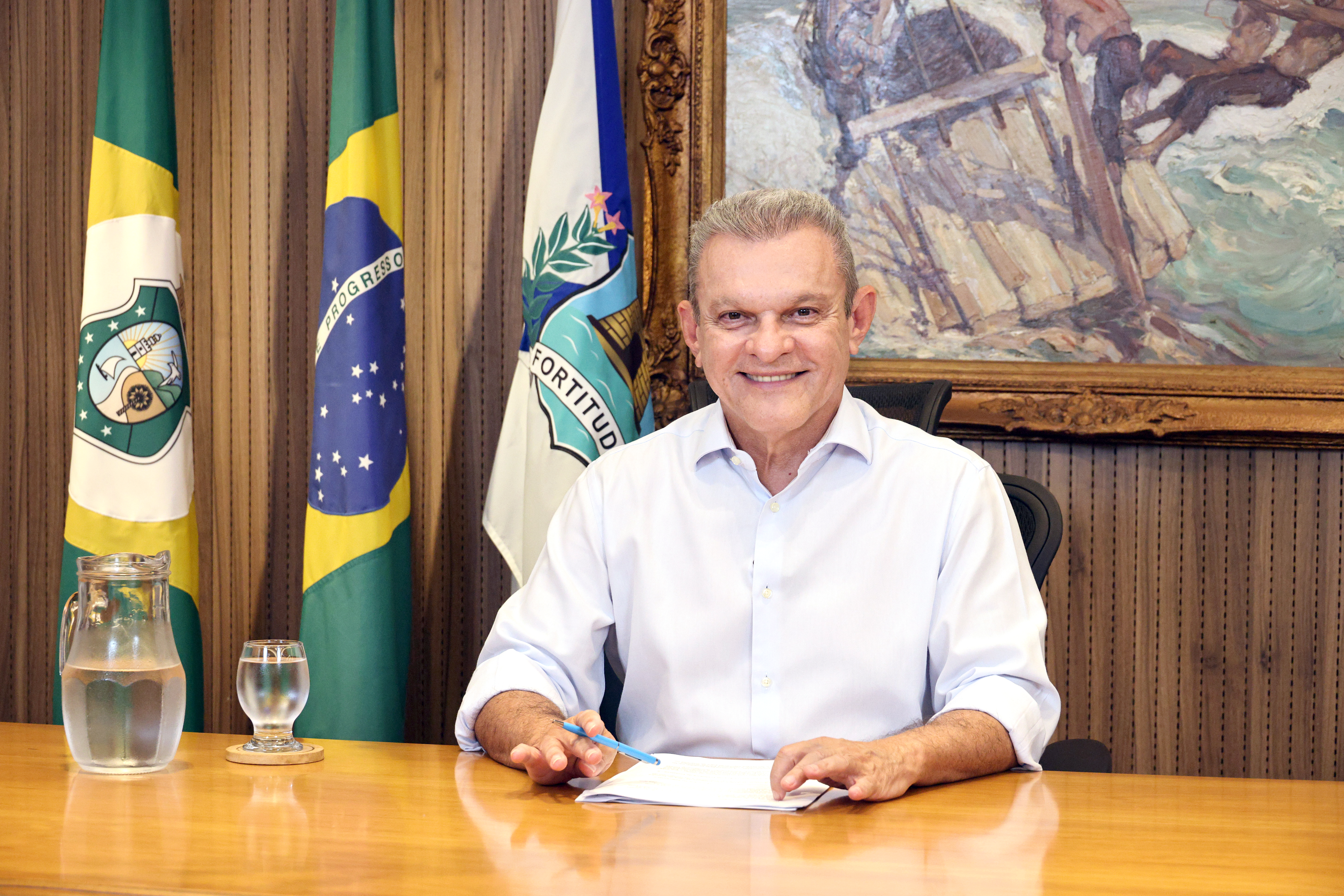 prefeito sentado com as mãos em cima da mesa segurando um papel